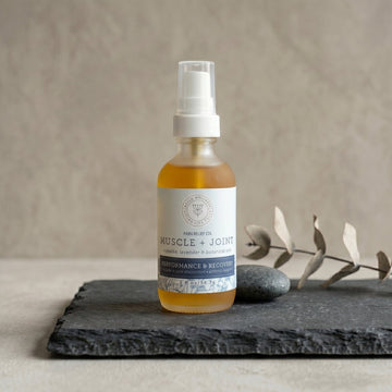 Bottle of 'Muscle + Joint' pain relief oil on a dark surface with a neutral background