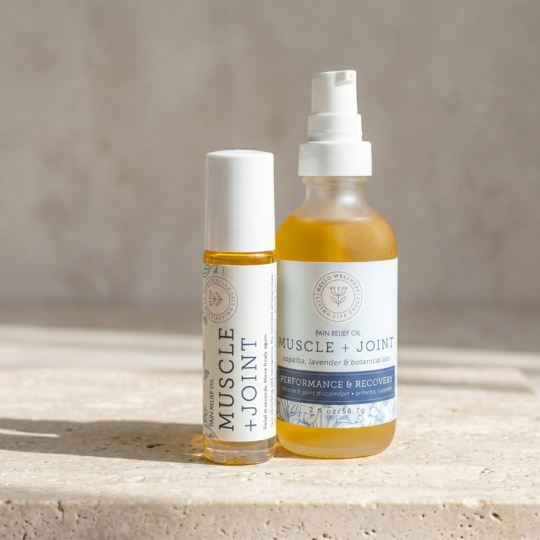 Two bottles of Muscle + Joint Pain Relief Oil on a stone surface with a neutral background. Hello Wellness