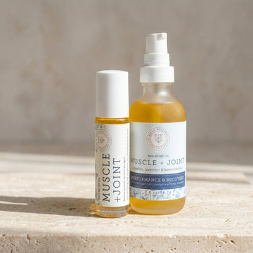 Two bottles of Muscle + Joint Pain Relief Oil on a stone surface with a neutral background. Hello Wellness