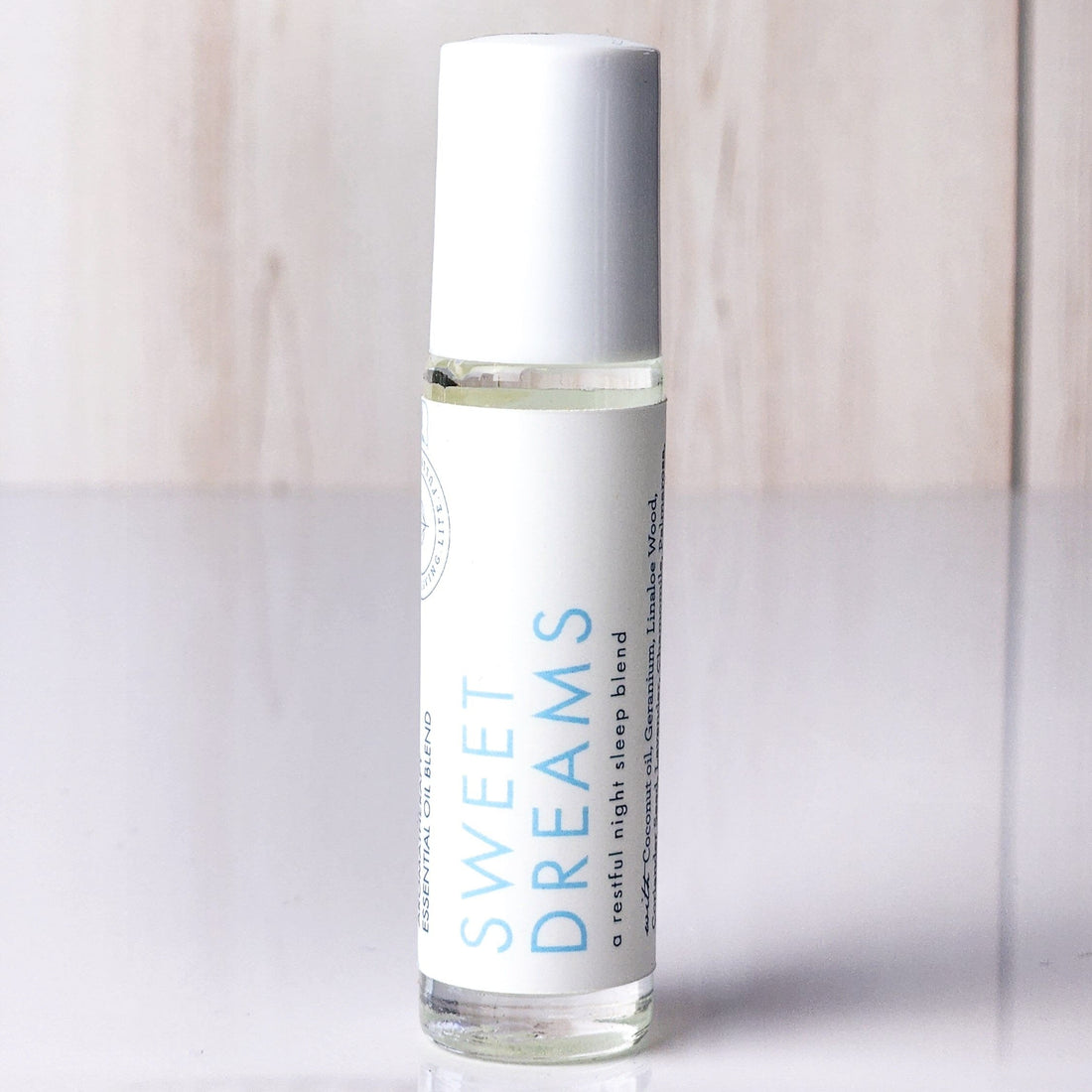 Five clear glass roll-on bottles with white caps and white labels are arranged on a light neutral surface. The labels read Citrus Spice, Unwind, Energize, Calm Belly, Deep Breath, and Sweet Dreams.