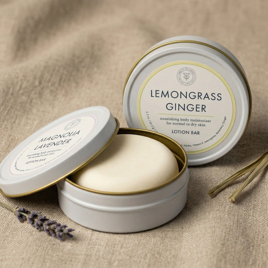Two tins of lemongrass ginger and magnolia lavender lotion bars on a textured surface.