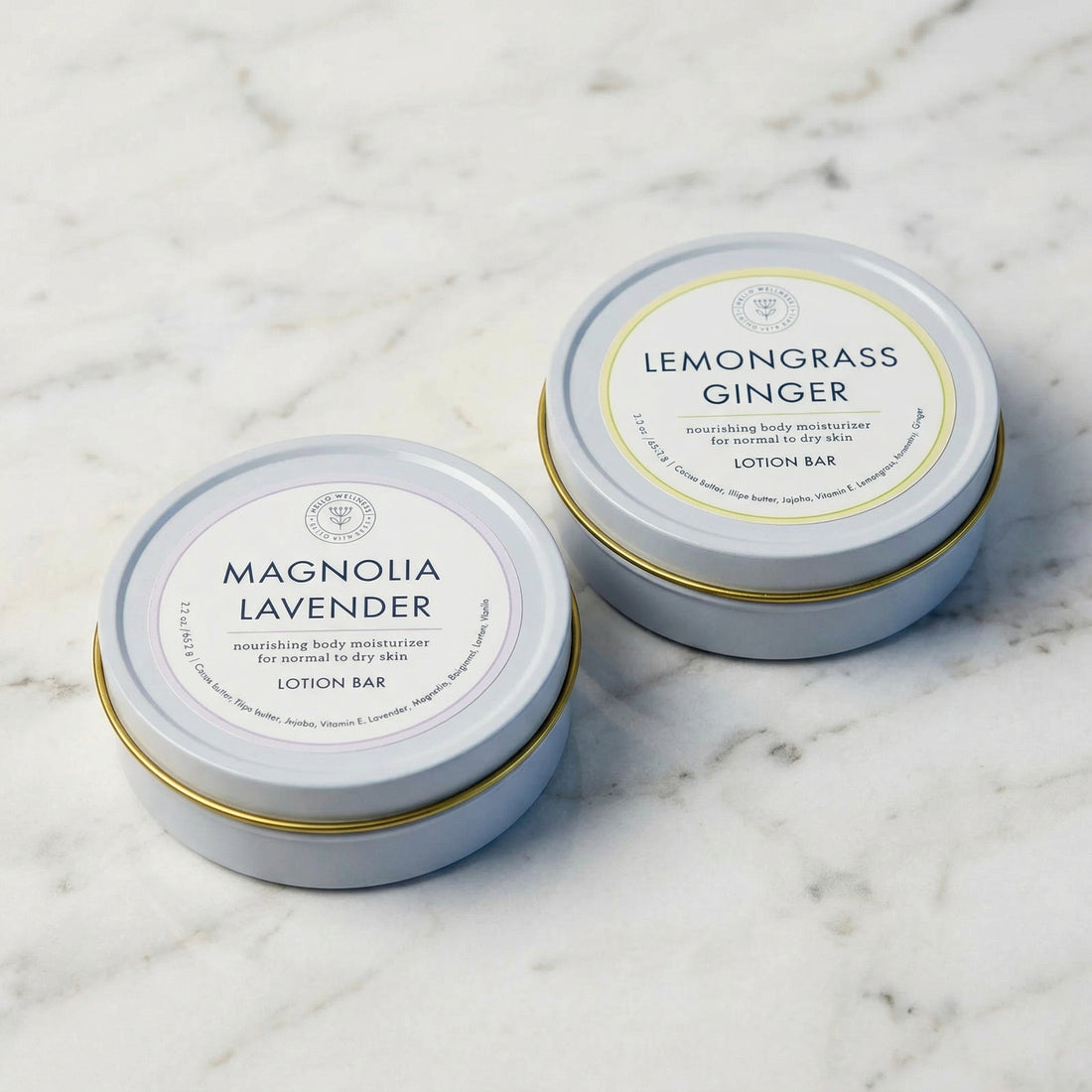 Two tins of lemongrass ginger and magnolia lavender lotion bars on a textured surface.