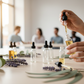 Minimal close-up of hands filling clear glass rollerball bottles with essential oils. Clean wooden table, droppers, soft botanicals. Bright natural light, modern wellness studio, diverse participants softly out of focus.