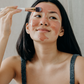 Woman applying a pink clay facial mask to her forehead with a brush as part of her skincare routine.