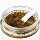 Open jar of Lemongrass + Ginger Body Scrub. Exfoliates & moisturize dry, dull skin with sea salt & poppy seeds & shea butter.