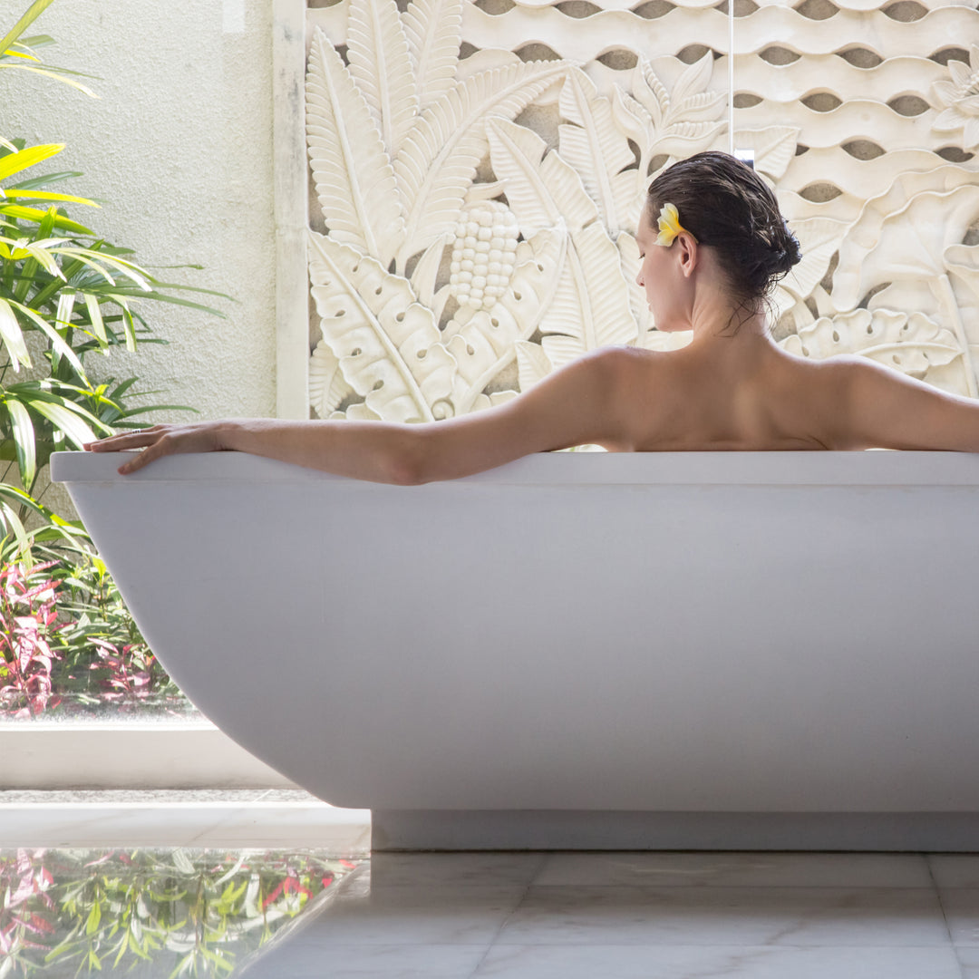 Woman soaking in a tub enjoying a coconut milk bath with, calm bath soak & flower petals. Perfect for resetting the body.