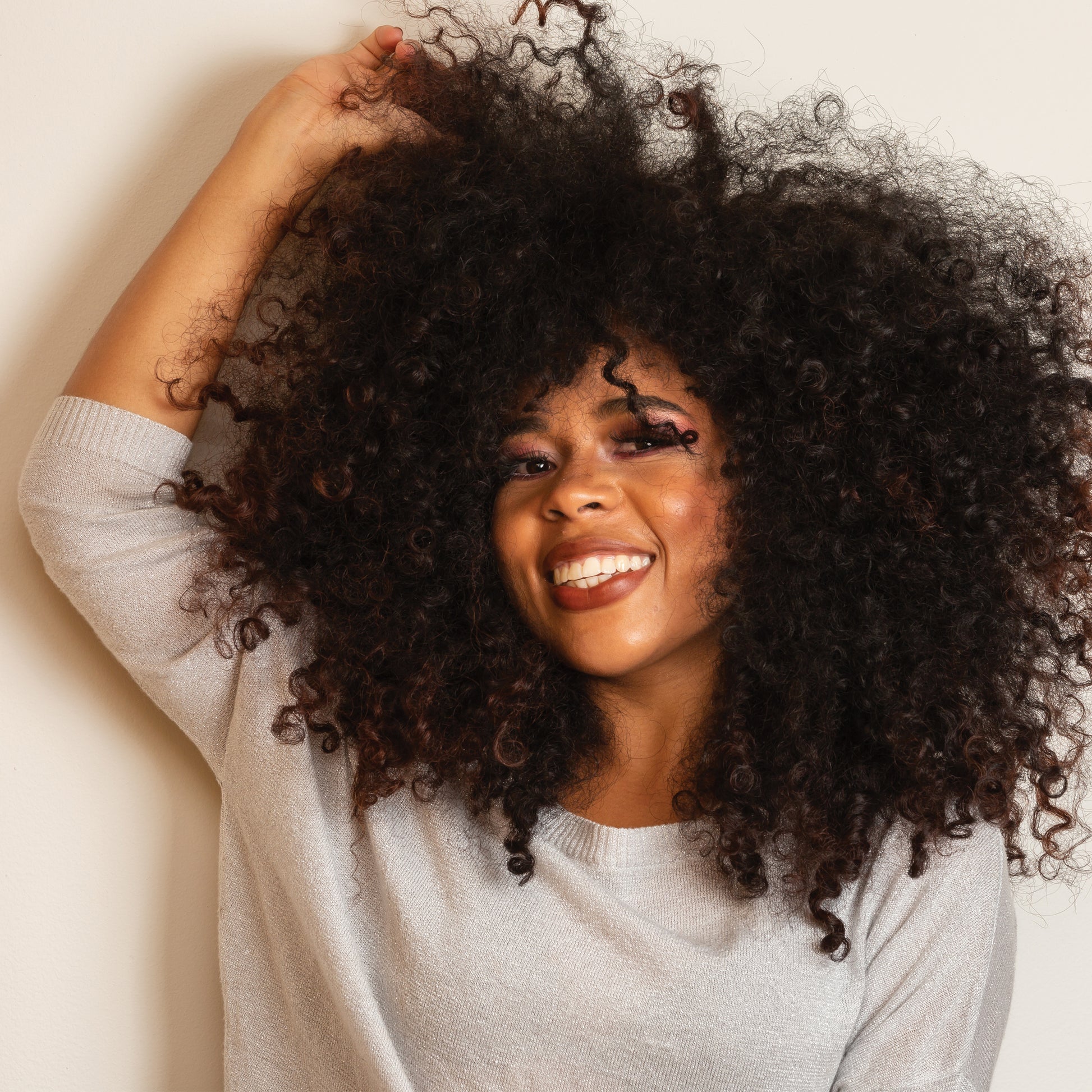 African American woman playing with her natural & curly hair. Intensely Moisturizing Hair Growth Oil Hello Wellness.